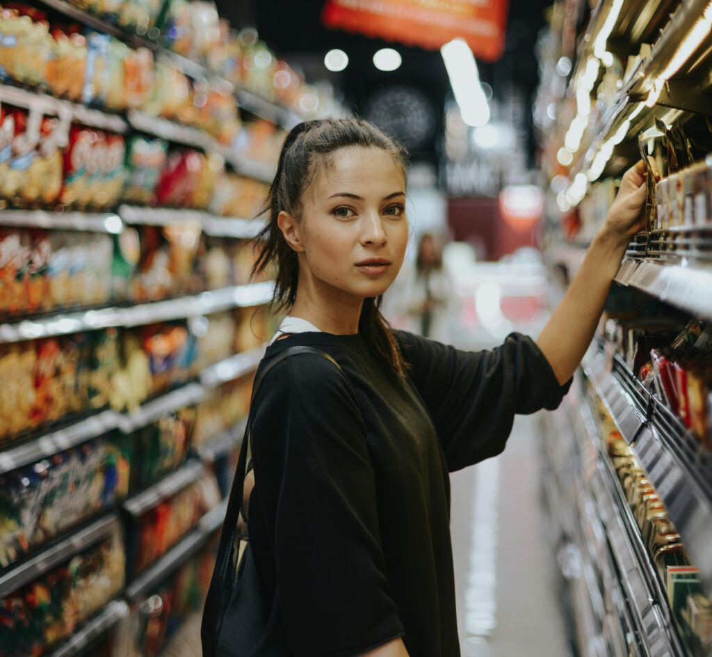 A shopper selecting a product from a retail display aisle, illustrating consumer decision-making and in-store purchasing behaviour