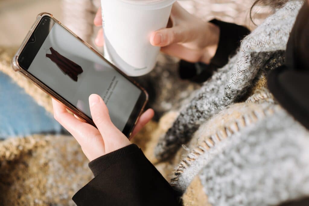 A shopper browsing a dress on a mobile phone while holding a coffee cup, illustrating the casual, distracted environment that ecommerce attention analysis must measure.