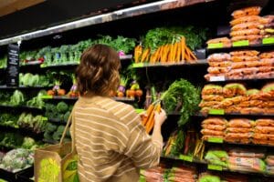 A shopper using a reusable bag to buy fresh produce in a supermarket, illustrating how to support the accelerating sustainability requirements of consumers.