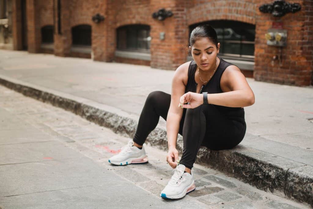 A runner checking her smartwatch on a city curb, demonstrating how visible progress drives subconscious consumer habits.