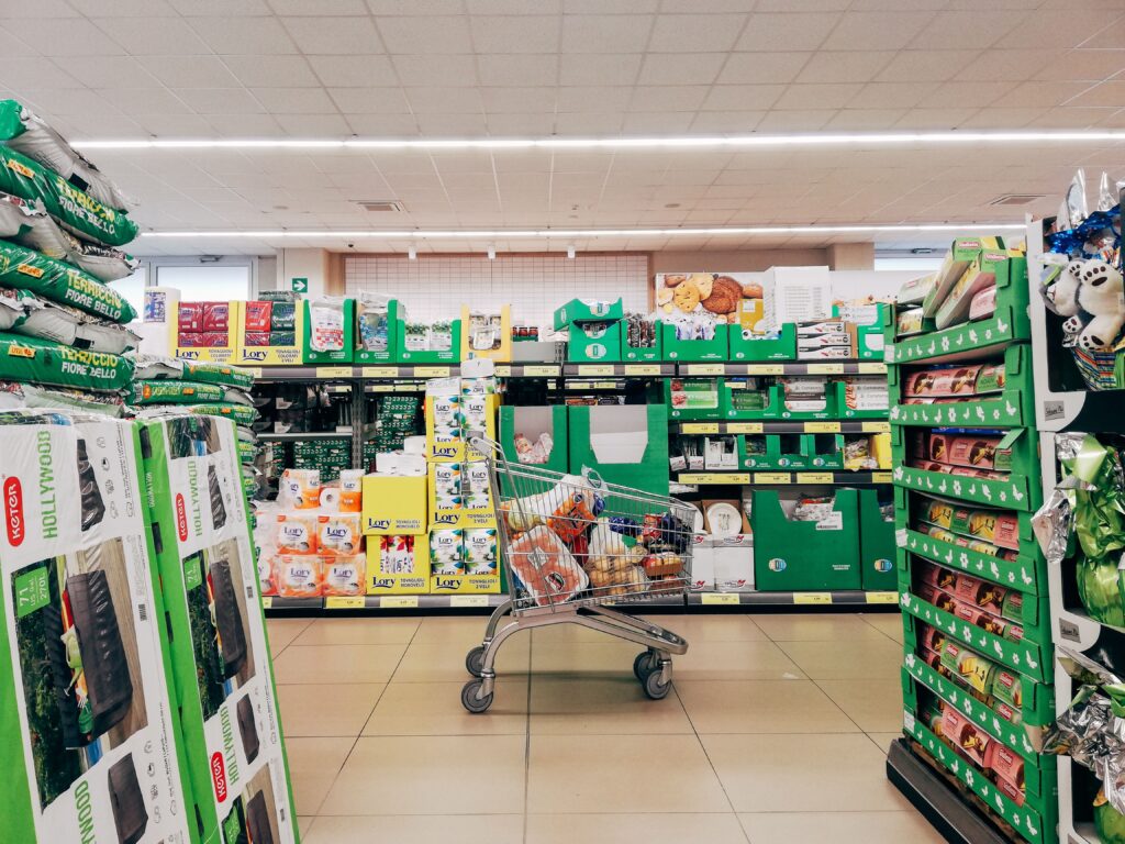 A discounter supermarket aisle featuring green shelf-ready packaging and a shopping trolley, illustrating processing fluency and own-label retail strategy.